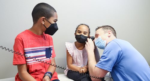 Dr. Fayed of Community Health Partners laughs as he pretends to examine a little girl's ear. Her brother sits next to her